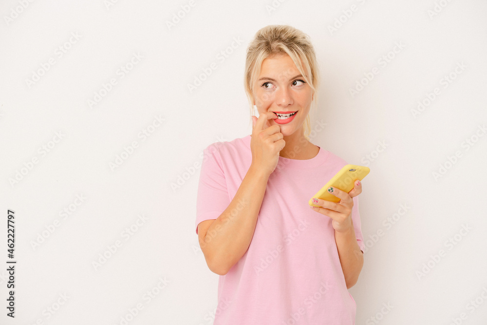 Young Russian woman holding mobile phone isolated on white background relaxed thinking about something looking at a copy space. Young Russian woman holding mobile phone isolated on white background relaxed thinking about something looking at a copy space.