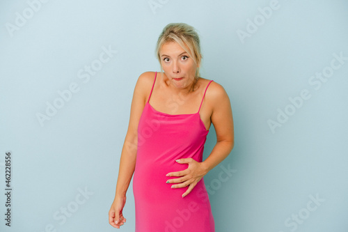 Young Russian woman pregnant isolated on blue background shrugs shoulders and open eyes confused.
