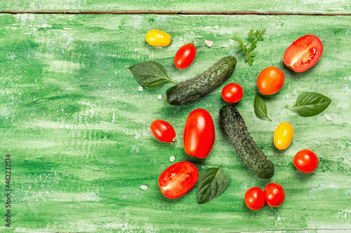 Fresh tomatoes  cucumbers  and basil leaves. Ripe vegetables on a green wooden background