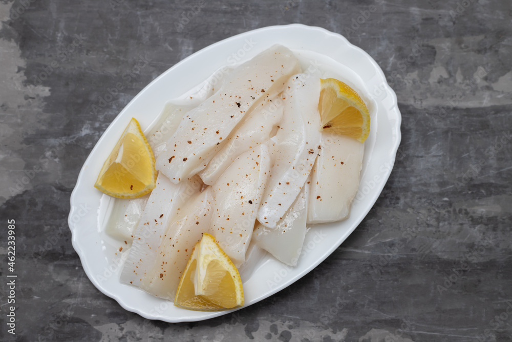 raw squid with pepper and fresh lemon on white dish raw squid with pepper and fresh lemon on white dish