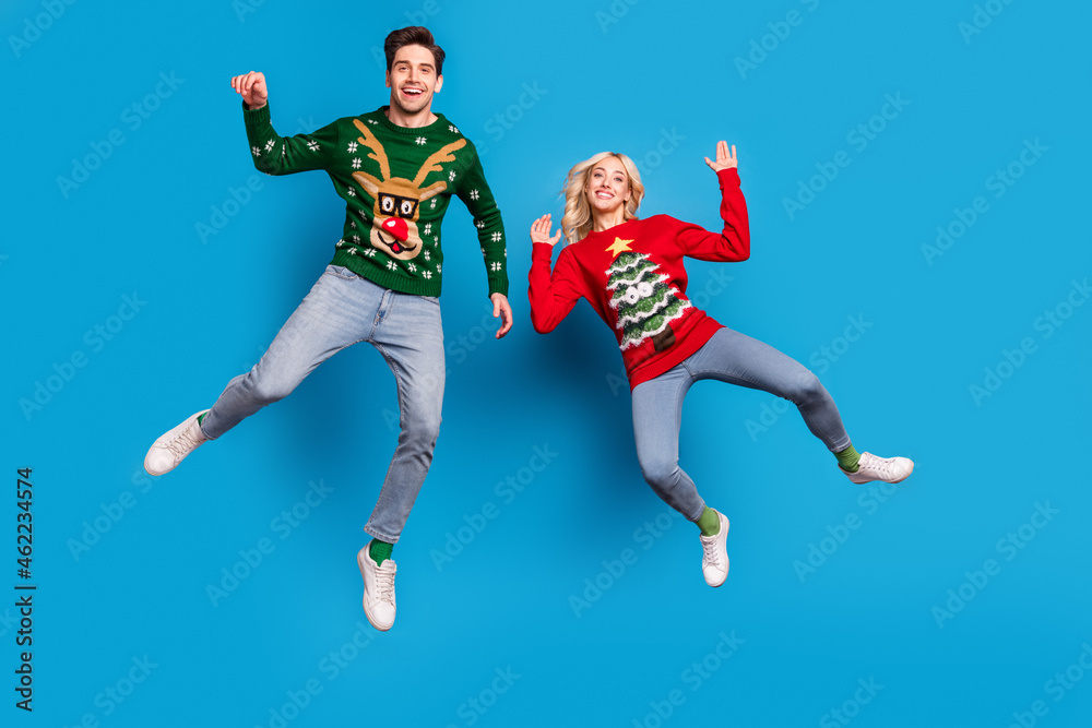 Obraz premium Photo of pretty cheerful young couple dressed ugly print sweaters smiling jumping high isolated blue color background