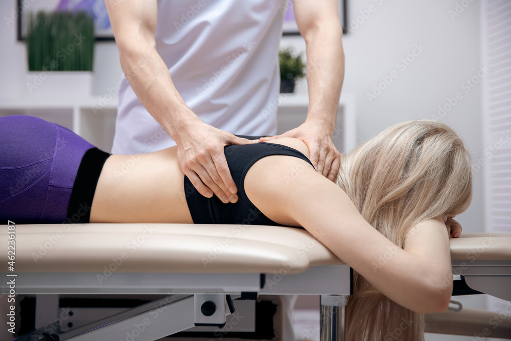 Doctor performs sports massage back neck therapy for young woman athlete after workout Doctor performs sports massage back neck therapy for young woman athlete after workout
