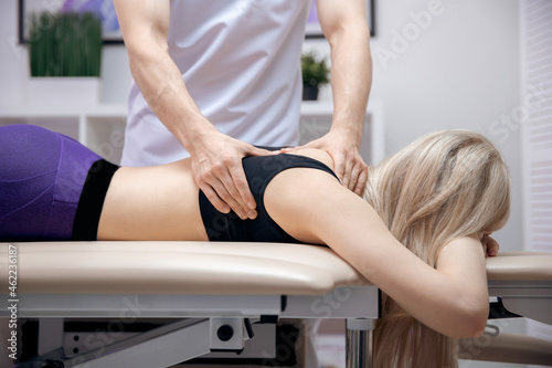 Doctor performs sports massage back neck therapy for young woman athlete after workout