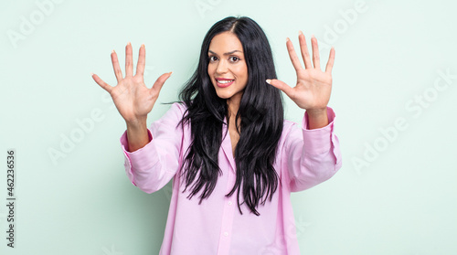 pretty hispanic woman smiling and looking friendly, showing number ten or tenth with hand forward, counting down photo