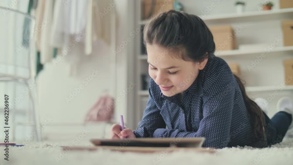 Joyful Schoolgirl Teenage Girl Studying, Doing Homework, Taking Notes Using Tablet on the Floor in her Room. Comfortable Home Distance Learning. E-learning Process, Application Use Concept. Joyful Schoolgirl Teenage Girl Studying, Doing Homework, Taking Notes Using Tablet on the Floor in her Room. Comfortable Home Distance Learning. E-learning Process, Application Use Concept.