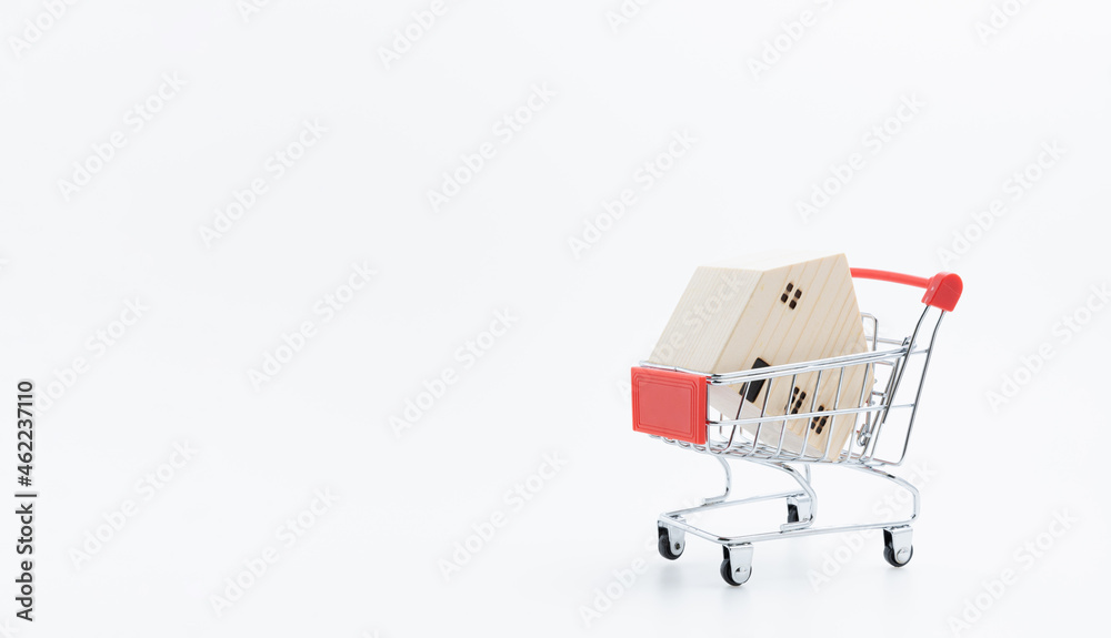 A little model wooden house in a shopping cart on white background with copy space. Shopping online, and house sale concept. Investment of estate property.