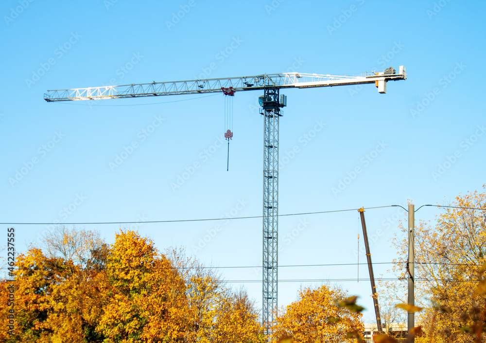 Construction crane and trees in autumn. Blue skies. Electricity cables.