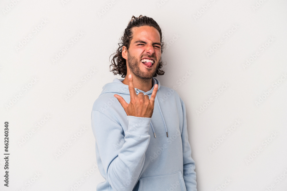 Young caucasian man isolated on gray background showing rock gesture with fingers Young caucasian man isolated on gray background showing rock gesture with fingers