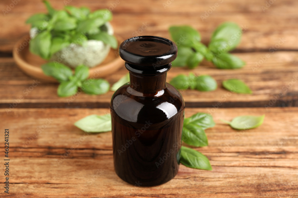 Glass bottle of basil essential oil and leaves on wooden table