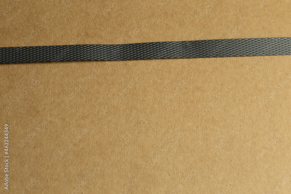 Fototapeta premium Package of brown cardboard with slightly slanted single dark gray parcel tape photographed in oblique close-up with bokeh in background and foreground