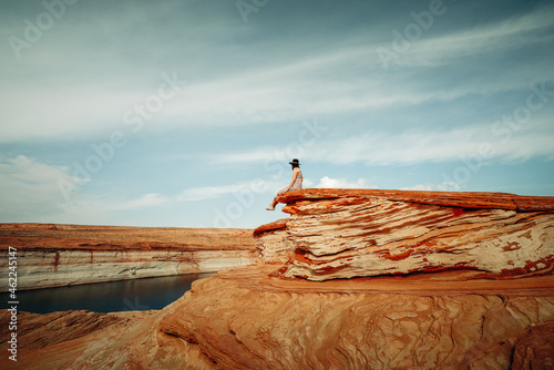 Woman sitting on a cliff top. Sandstone bluffs, lake Powell and cloudy sky background. Exploring The Chains,  Glen Canyon, Arizona