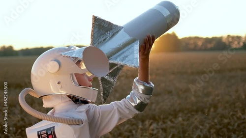 Little young happy cute child boy wearing astronaut uniform and helmet cosmonaut playing, launching toy rocket at sunset field, Space man, Kid dream flying, childhood, freedom, travel, future concept