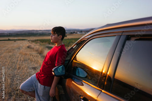 Teenage boy leaning against a car at sunset
