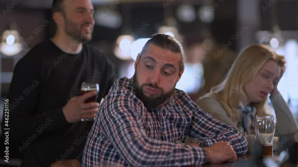 Dissatisfied Caucasian friends watching sport match in pub making disappointed facial expression as team loses. Side view of young men and woman fans in bar indoors with beer glasses sighing Dissatisfied Caucasian friends watching sport match in pub making disappointed facial expression as team loses. Side view of young men and woman fans in bar indoors with beer glasses sighing