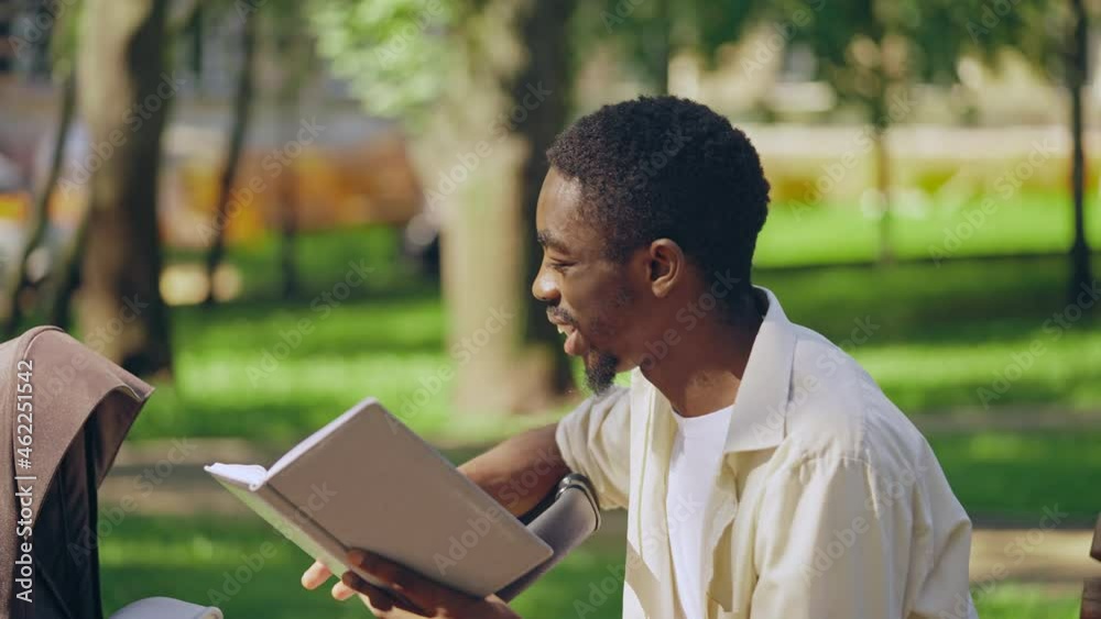 Happy young father reading book to baby, sitting on bench in park, togetherness Happy young father reading book to baby, sitting on bench in park, togetherness