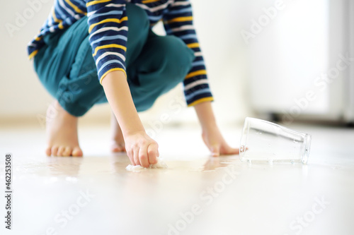 Foto Little boy wipes water spilled from a glass on the floor