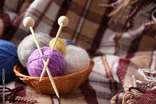 Multi colored balls of yarn with knitting needles in a wicker basket on the background of a plaid photo