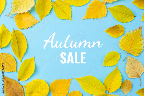 Words Autumn Sale. Wooden blocks with letters on blue background surrounded by yellow leaves. Fall shopping concept. Selective focus