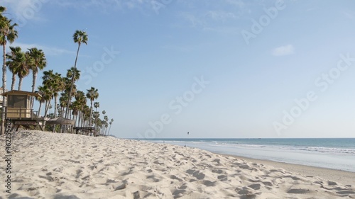 Tropical palm trees, white sandy beach by sea water wave, pacific ocean coast, San Clemente California USA. Blue sky and lifeguard tower. Life guard watchtower hut, summertime shore. Los Angeles vibes
