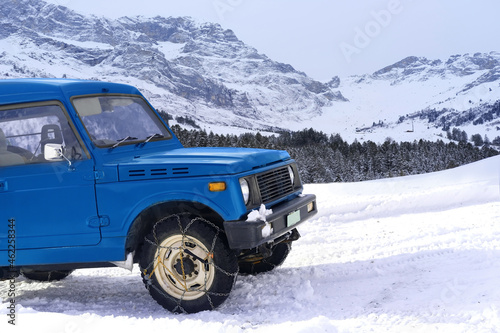 close-up of a blue SUV with iron chains on wheels against the background of the Alpine mountains, the concept of the safety of movement of cars with snow chains on tire on a winter road © kittyfly