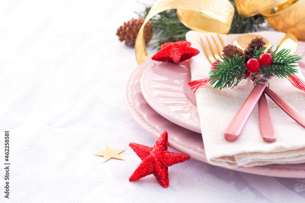 concept of christmas table setting. two pink plates and pink and gold cutlery with decor on a linen napkin. fir branches, cones and stars..