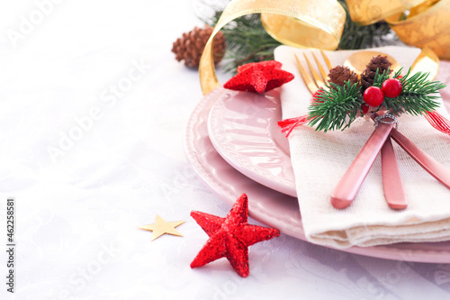 concept of christmas table setting. two pink plates and pink and gold cutlery with decor on a linen napkin. fir branches, cones and stars..