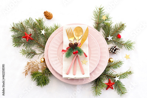 concept of christmas table setting. two pink plates and pink and gold cutlery with decor on a linen napkin. fir branches, cones, balls and stars..