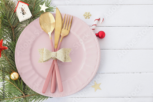 Christmas table setting in white-pink-gold colors. pink plate, cutlery with gold bow, fir branches, snowflakes and stars. Copy space..