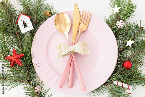 Christmas table setting . pink plate, cutlery with gold bow, fir branches, snowflakes and stars..