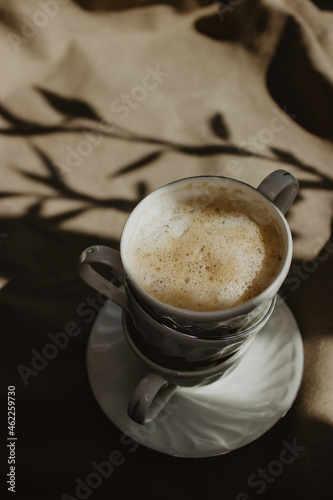 Modern coffee cup with milk and foam on a beige background isolated with a plant shadow and a cloth napkin.