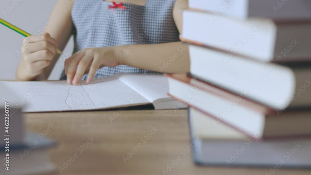 Close up and candid of kid hands who is writing on paper book on table seriously with stacks of books as foreground. Unrecognised girl is learning for education development and creative imagination. Close up and candid of kid hands who is writing on paper book on table seriously with stacks of books as foreground. Unrecognised girl is learning for education development and creative imagination.
