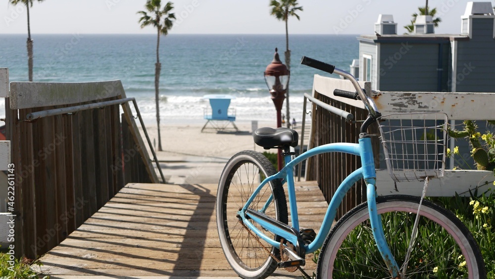 Blue bicycle, cruiser bike by ocean beach, pacific coast, Oceanside California USA. Summertime vacations sea shore. Vintage cycle by wooden stairs, stairway or staircase. Tropical palms and lifeguard Blue bicycle, cruiser bike by ocean beach, pacific coast, Oceanside California USA. Summertime vacations sea shore. Vintage cycle by wooden stairs, stairway or staircase. Tropical palms and lifeguard