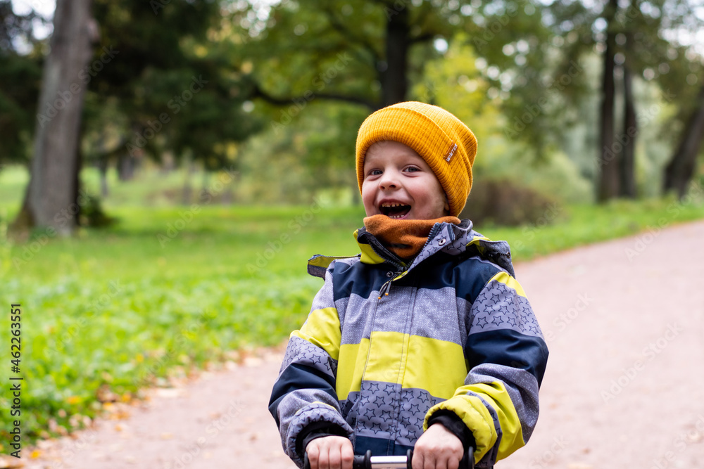 A child rides a scooter in an autumn park. A little boy in a yellow hat rejoices, smiles, laughs, walks in the forest in autumn A child rides a scooter in an autumn park. A little boy in a yellow hat rejoices, smiles, laughs, walks in the forest in autumn