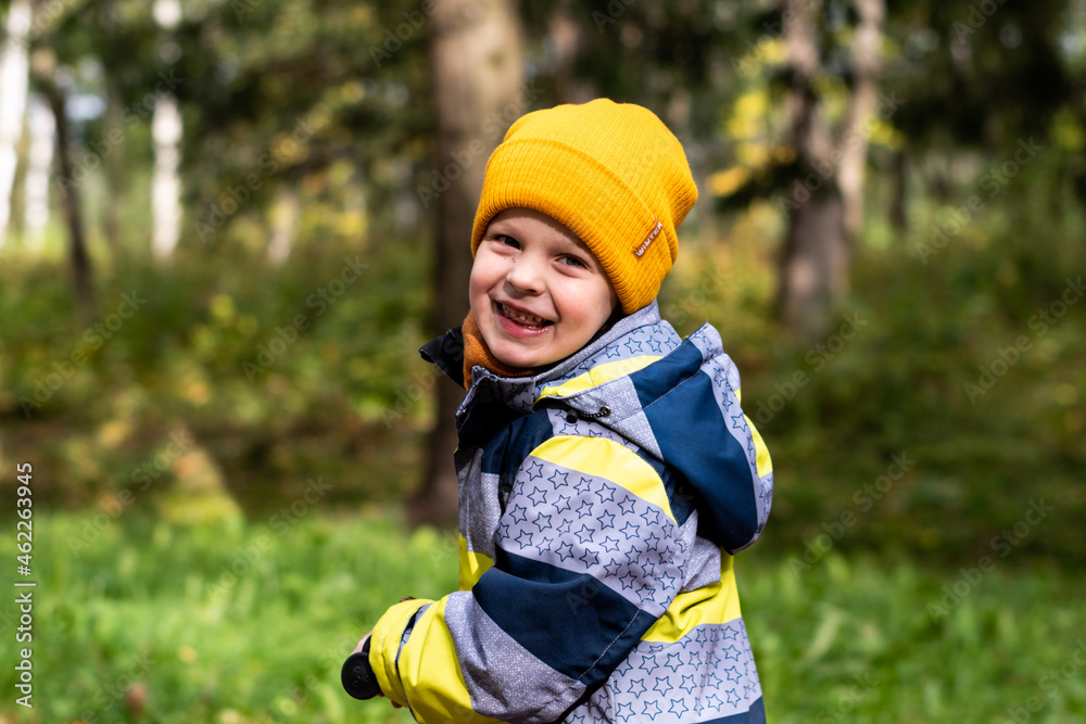 A child rides a scooter in an autumn park. A little boy in a yellow hat rejoices, smiles, laughs, walks in the forest in autumn A child rides a scooter in an autumn park. A little boy in a yellow hat rejoices, smiles, laughs, walks in the forest in autumn