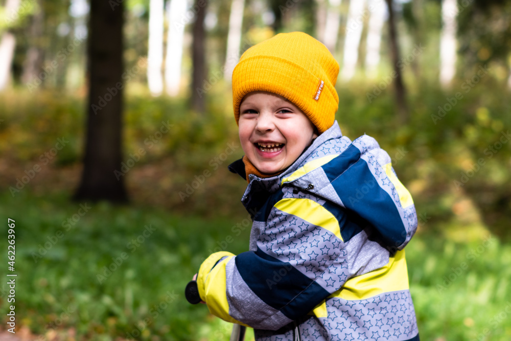 A child rides a scooter in an autumn park. A little boy in a yellow hat rejoices, smiles, laughs, walks in the forest in autumn A child rides a scooter in an autumn park. A little boy in a yellow hat rejoices, smiles, laughs, walks in the forest in autumn