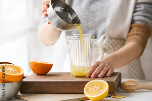 Woman making fresh citrus juice at table in kitchen