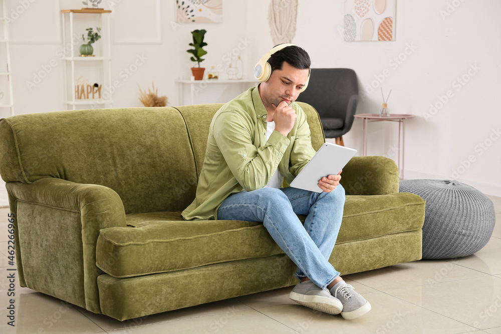Obraz premium Young man with tablet computer listening to audiobook at home