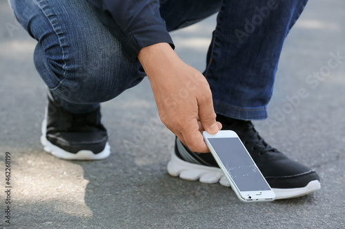 Man picking damaged mobile phone from pavement outdoors, closeup