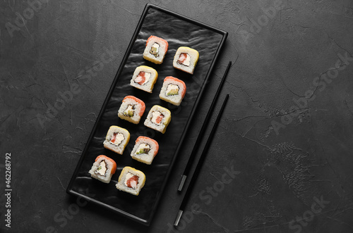 Board with delicious sushi rolls and chopsticks on dark background
