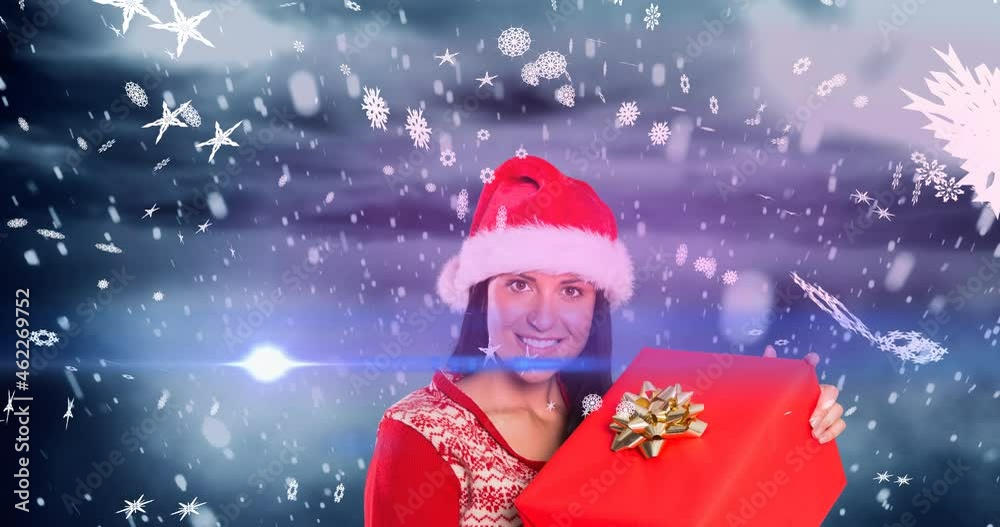Animation of snow falling over happy caucasian woman wearing santa hat keeping present Animation of snow falling over happy caucasian woman wearing santa hat keeping present
