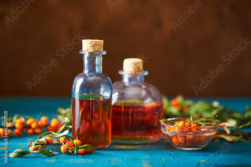 Glass bottle with sea buckthorn oil berries and sea buckthorn branches on wooden background