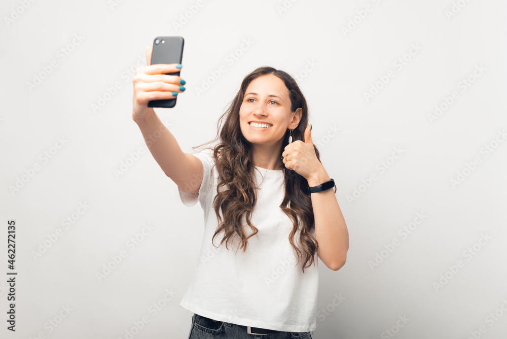 Beautiful woman is taking a selfie with her phone while showing thumb up.