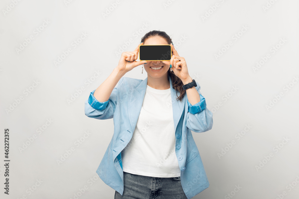 Playful businesswoman is covering her eyes with the screen of the phone she is holding. Playful businesswoman is covering her eyes with the screen of the phone she is holding.