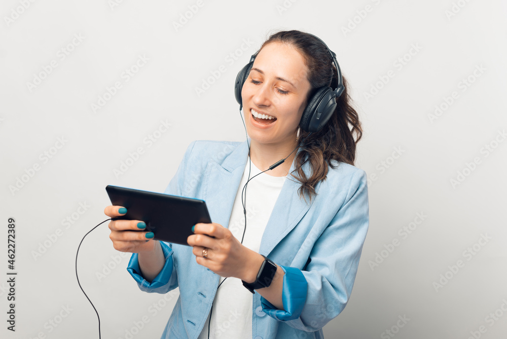 Smiling girl is wearing headphones and watching or playing something on the tablet she is holding. Smiling girl is wearing headphones and watching or playing something on the tablet she is holding.