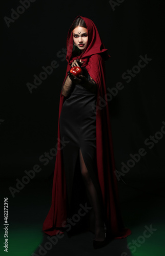 Young witch with apple on dark background