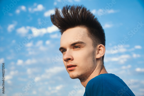 Outdoor portrait of teenager boy looking away with hair blowing in the wind against evening sky