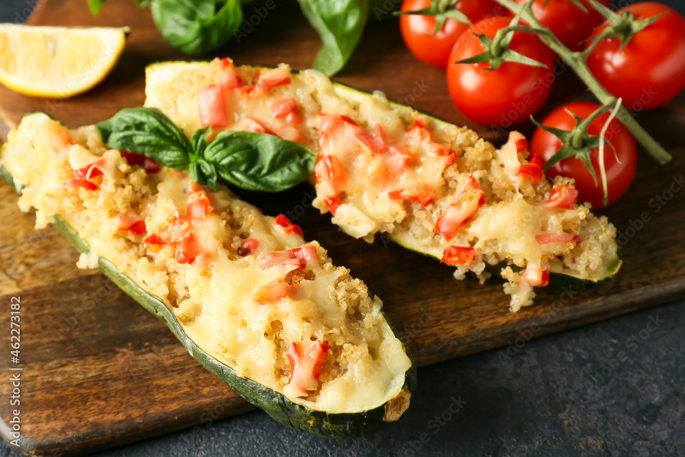 Wooden board with quinoa stuffed zucchini boats and fresh tomatoes on dark background