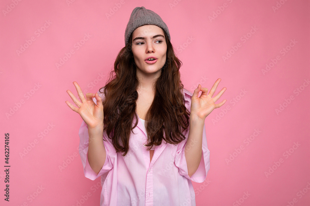 Beautiful pretty nice cute calm concentrated young curly brunette woman wearing pink shirt and grey hat isolated on pink background with copy space