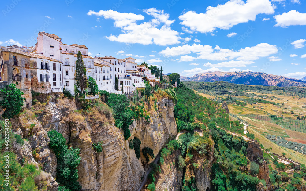 Ciudad antigua  de Ronda al borde del acantilado y el paisaje del valle de ronda con campo y montañas un día soleado con cielo azul y nubes desde Málaga, Andalucía, España.