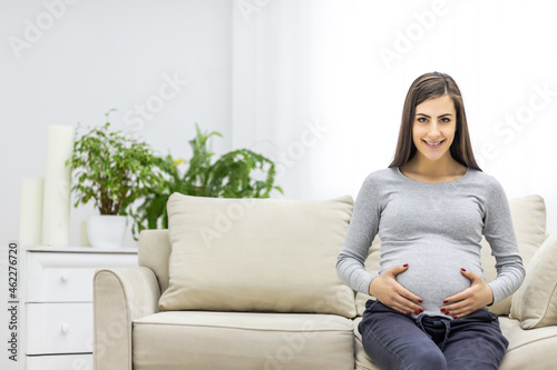 Photo of pregnant woman looking at camera and touching her stomach.